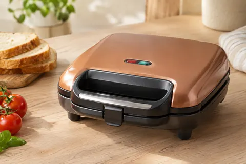 Appareil à croque-monsieur Bestron couleur cuivre avec poignée verrouillable sur un plan de travail clair.