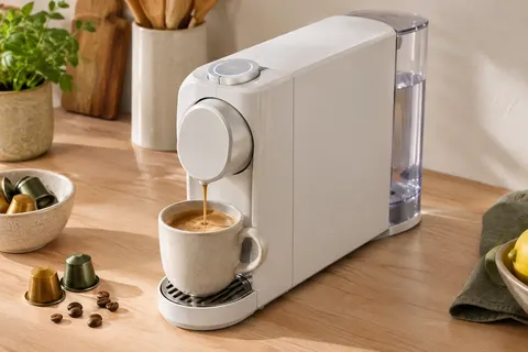 Machine à capsules blanche compacte sur un plan de travail en bois clair, avec molette LED visible